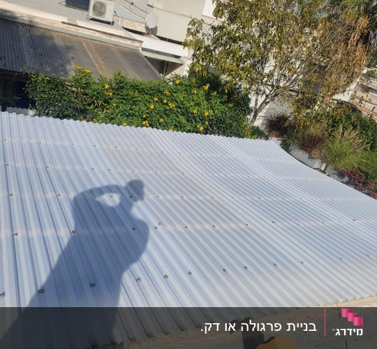 גג פלסטיק עם צל של אדם וצמחייה מסביב